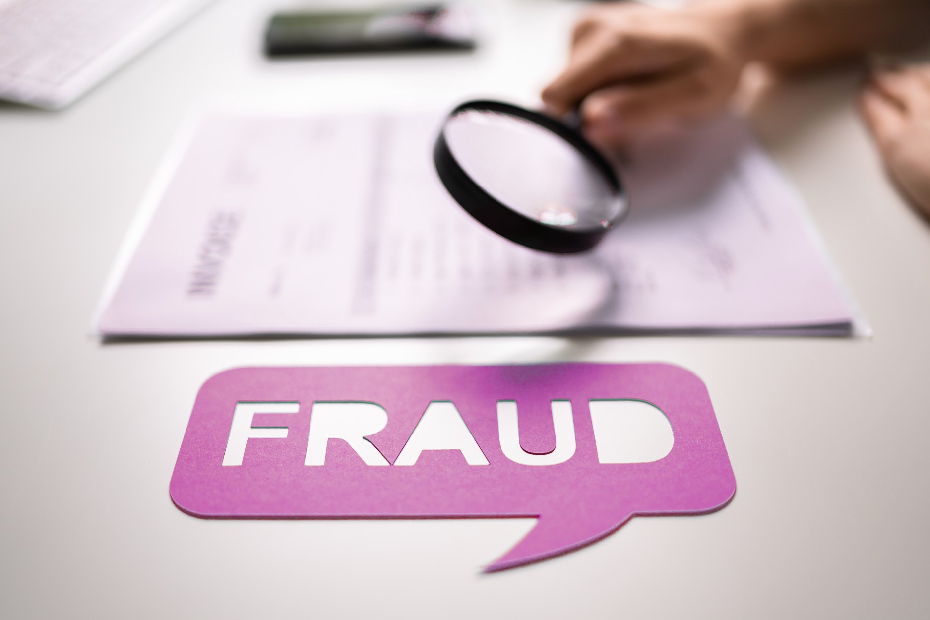 Magnifying glass examining a document with the word "fraud", illustrating document fraud detection and verification of document authenticity